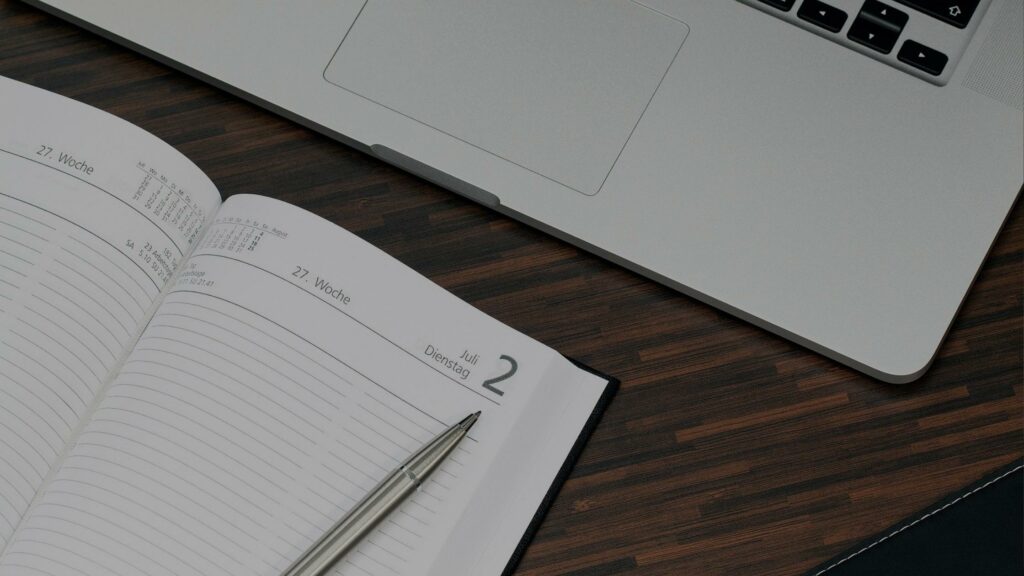 Diary lying open with pen on top next to laptop